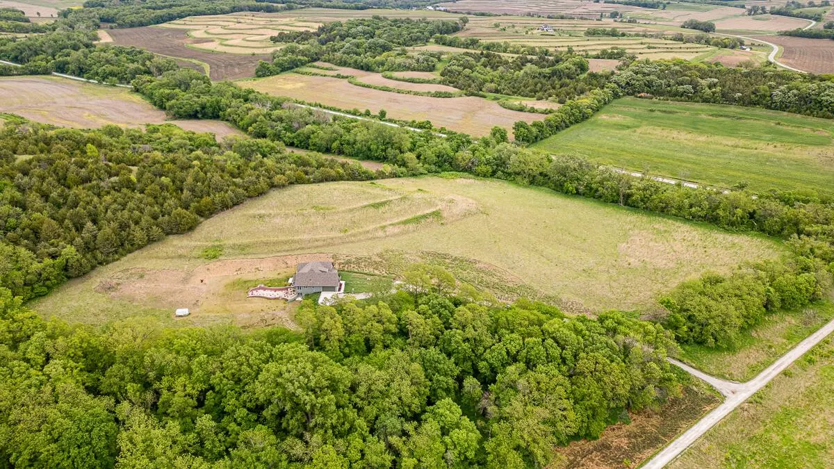 Aerial view of a custom-built home on a grassy hillside, surrounded by timber and terraced farm fields, on 240th Avenue near Thurman, Iowa